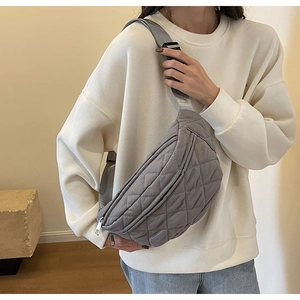 Close-up of grey quilted crossbody bag with adjustable strap worn by a model