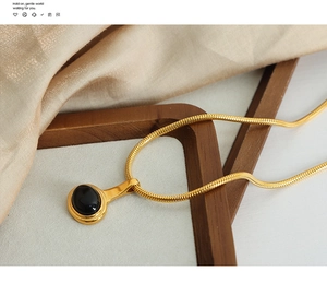 Macro detail of gold snake chain with a vintage oval black gemstone pendant on silk