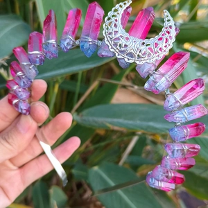 Pink and blue crystal crown with a hollow silver moon charm held over green foliage