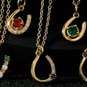U-shaped gold pendant necklace set with red, green, and blue stones on black background