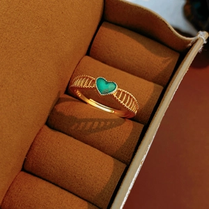 Détail macro d'une bague pierre verte en cœur avec filigrane doré dans un écrin velours