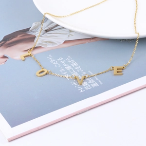 Detailaufnahme einer goldenen LOVE-Buchstabenkette auf minimalistischem Hintergrund