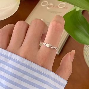Detail view of a silver heart and chain link ring worn on finger with soft lighting