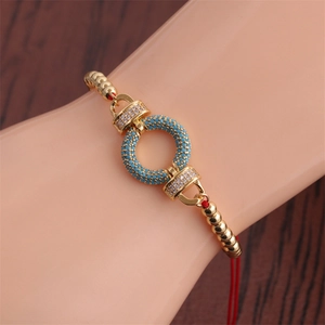 Detail of red rope bracelet with gold beads and a blue zircon encrusted ring charm