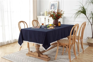 Detail of navy blue cotton tablecloth with white pom-pom fringe in a bright dining room