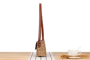 Side view of woven straw shoulder bag with brown leather flap and metal rivet details