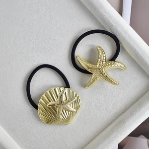 Detail of high-stretch hair ties with gold alloy starfish and seashell charms on a tray