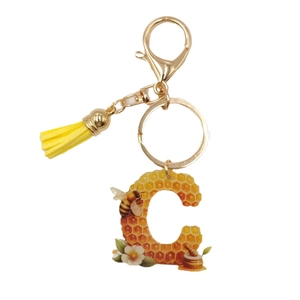 Letter C keychain with honeycomb pattern, yellow tassel and golden clasp on white background