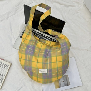 Detail of yellow plaid canvas hobo bag with large capacity next to a laptop