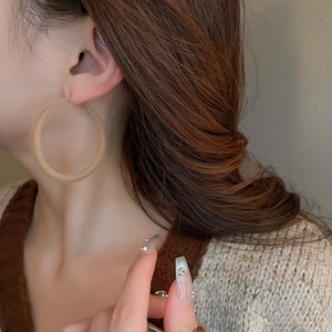 Close-up of a model wearing large khaki flocked geometric hoop earrings in a retro style