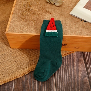 Close-up of dark green knit baby sock featuring a mini Christmas tree ornament on cuff