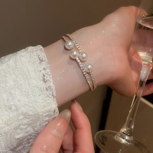 Détail d'un élégant bracelet double couche doré avec quatre perles et diamants scintillants