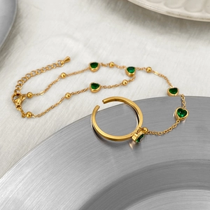 Detail of golden hand harness featuring green heart gemstone on a brushed metal tray