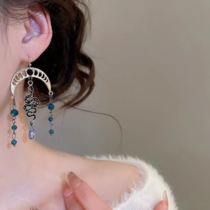 Detailed view of silver snake and moon earrings with blue crystal tassel on model
