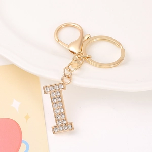 Close-up of golden metal letter I keychain pendant with sparkling rhinestones on ceramic