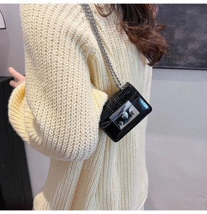 Detail showing a micro black crossbody chain bag worn on a cream knit sweater
