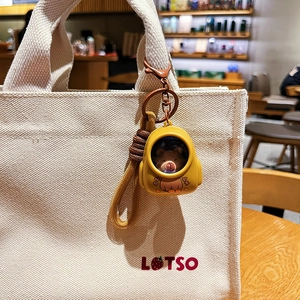 Cute brown bear astronaut keychain in yellow space suit on a beige canvas bag