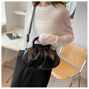 Detail of black pleated cloud bag with detachable strap worn by model in a cafe setting