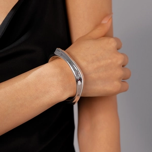 Close-up of wavy wide silver metallic cuff bracelet with high polished reflective finish