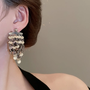Detail view of silver tiered sequin tassel earrings worn by a model to show drape and scale