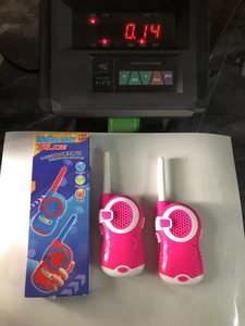 Pink walkie talkie toy set with packaging shown on a digital scale for weight check