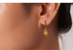 Close-up of 18k gold celestial sun charm earrings featuring a detailed face engraving