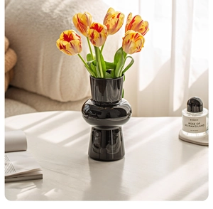 Detail of a sleek black ceramic gourd vase with vibrant tulips in a home setting