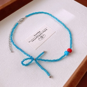 Blue beaded necklace with bow design and red accents on a cream jewelry tray