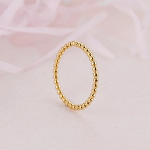 Bague perlée minimaliste en acier titane plaqué or pour femme sur fond rose doux