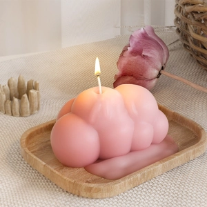 Dettaglio di una candela rosa a forma di nuvola accesa su un vassoio di legno decorato