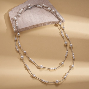 Detail view of double-layered pearl necklace with silver chain on textured stone