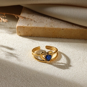 Macro detail of a double-layered gold open heart ring with a blue gemstone on a stone block