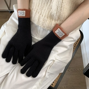 Close-up of black knitted gloves with brown ribbed cuffs and a decorative sewn-on label
