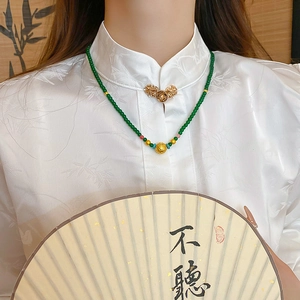 Detail of Chinese emerald bead necklace with gold filigree pendant worn on white shirt