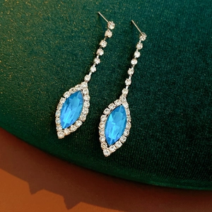 Detailed macro view of sparkling blue crystal drop earrings on green velvet surface
