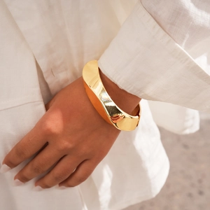 Detailed view of wide twisted gold metal cuff bracelet with a polished mirror finish