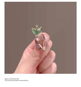Close-up of pink and green crystal carrot brooch with faceted surface on gold metal base