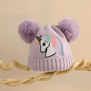 Detail der lila Einhorn-Strickmütze für Mädchen mit zwei flauschigen Bommeln und Stickerei