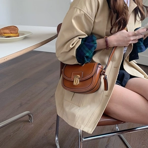 Dettaglio borsa a sella in pelle marrone con fibbia in metallo e tracolla su una modella