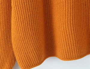 Détail du pull en maille orange montrant la texture côtelée et les coutures de l'ourlet