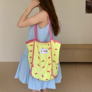 Side view of a large yellow plaid tote bag with bow prints and pink shoulder straps