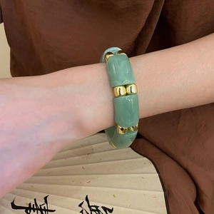 Close-up of green bamboo-shaped acrylic beads and gold spacers on an elastic bracelet