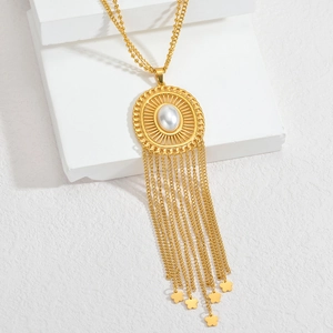 Bohemian gold tassel necklace with a pearl pendant and metal flowers on a white stand
