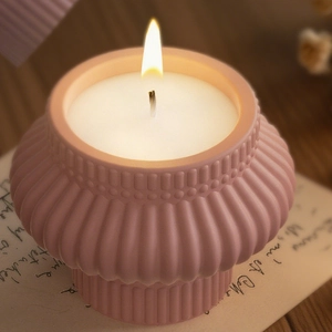 Scented candle in pink pleated ceramic jar with burning flame on vintage background