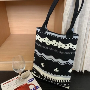 Close-up of a knit tote bag with black and white geometric floral patterns near a bookshelf