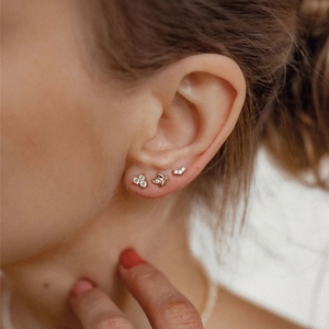 Close-up of three gold earrings featuring butterfly and diamond cluster designs on ear