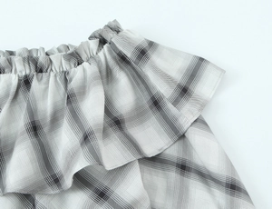 Detail showing elastic off-shoulder neckline and ruffled trim of black plaid blouse