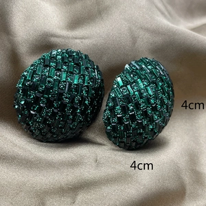 Close-up of 4cm chain-link earrings with vibrant green crystals on champagne satin