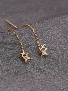 Macro shot of long gold tassel earrings with zircon-inlaid star charms on gray fabric
