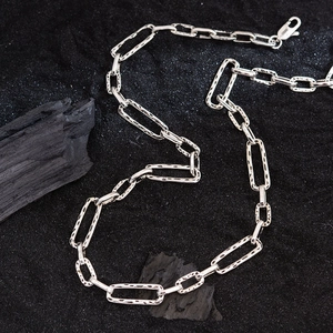 Minimalist silver paperclip chain necklace with textured links over black sand